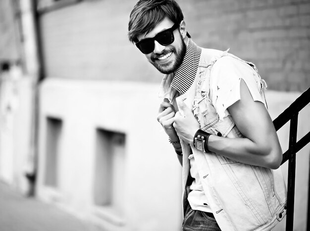 Funny smiling hipster handsome man guy in stylish summer clothes posing in the street