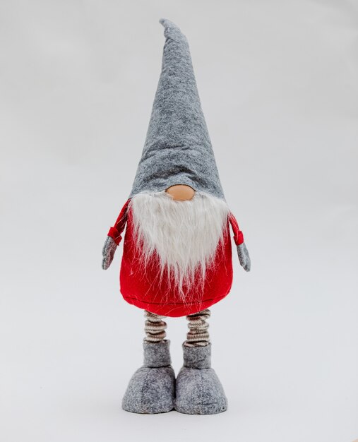 Funny soft Christmas toy in the shape of a gnome in a red coat and gray cone-shaped cap