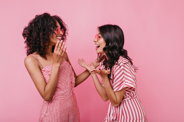 Funny story made two friends laugh heartily. Portrait of girls in pink striped outfits who are having fun.
