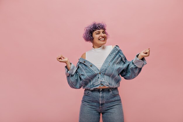 Funny stylish lady with snow-white smile has fun on pink. Woman in jeans tight pants.