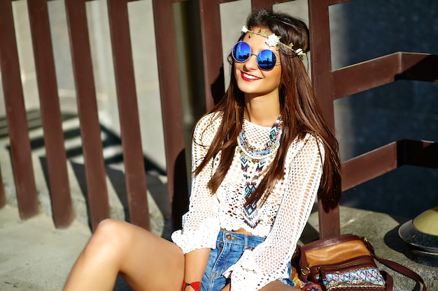 Funny stylish sexy smiling beautiful young hippie woman model in summer white hipster clothes posing in the street