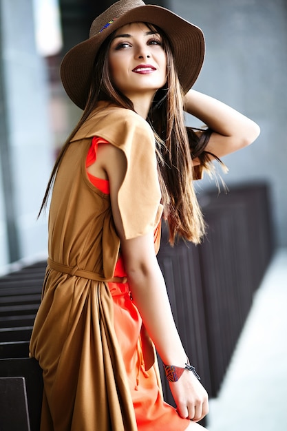 夏の明るい流行に敏感な服で面白いスタイリッシュなセクシーな笑みを浮かべて美しい若いヒッピー女性モデルの帽子の通りのドレス