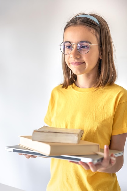 Funny teen girl with books and laptop on the background of a white wall