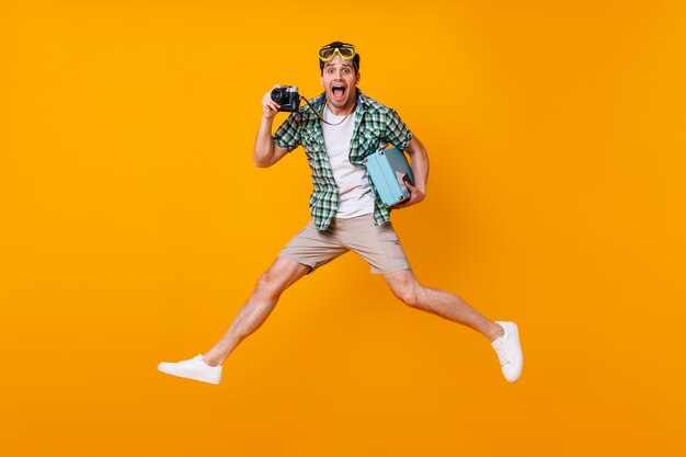 레트로 카메라와 파란색 가방을 들고 여름 옷에 재미있는 관광 남자. 오렌지 공간에 점프 다이빙 마스크에 남자입니다.