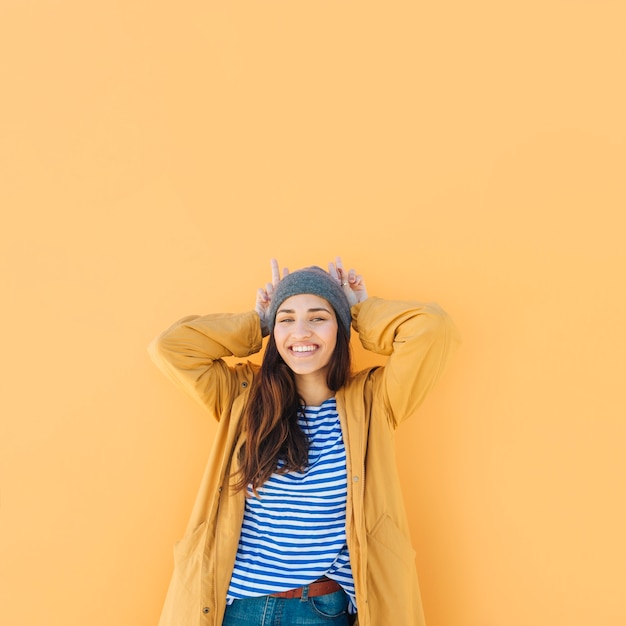 funny woman making horn with hands looking at camera against plain background