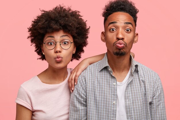 Funny woman and man keeps lips round, make grimace, stand next to each other, dressed casually