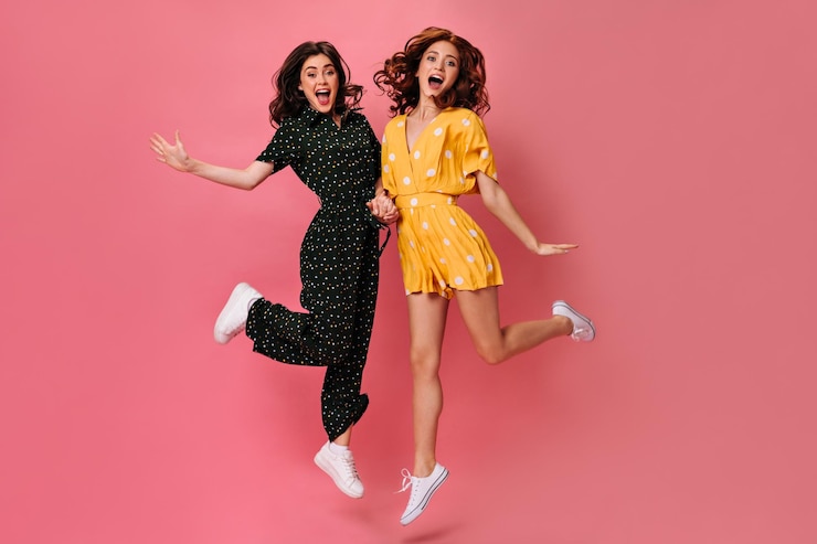 Free Photo funny women happily jump on pink background charming ladies in cool polka dot clothes and with curly dark hair have fun