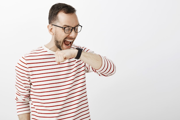 Funny yelling european man in glasses, raising arm near face and shouting at black digital watch, making command to personal assistant or talking with client via device