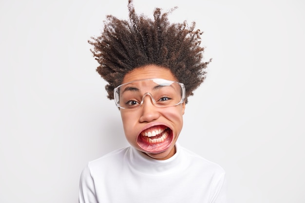 Funny young afro american woman has wide opened mouth wears transparent glasses, exclaims loudly.