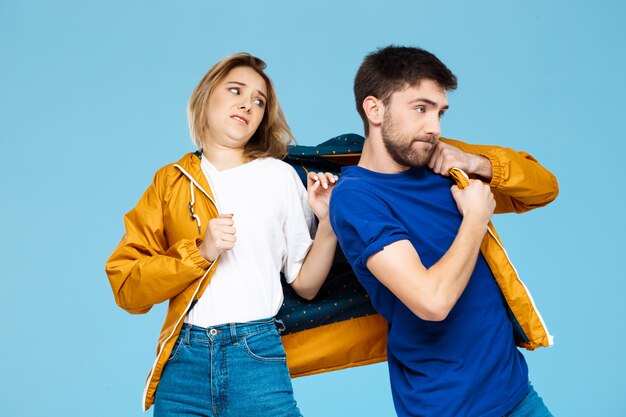 funny young beautiful couple wearing one jacket  over blue wall