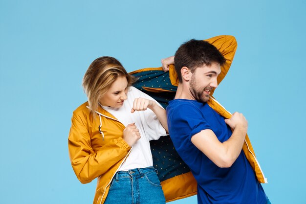 funny young beautiful couple wearing one jacket  over blue wall