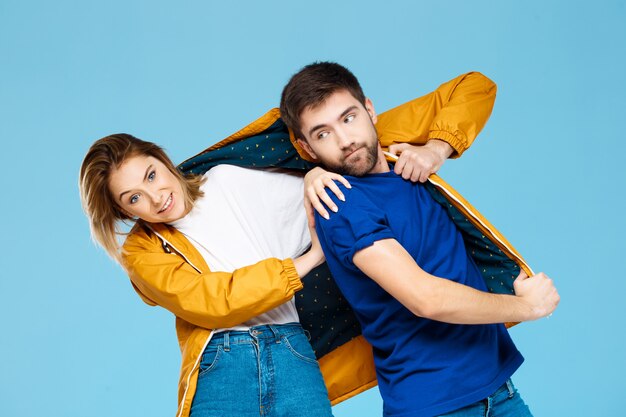 funny young beautiful couple wearing one jacket  over blue wall