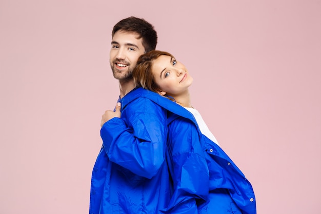 Funny young beautiful couple wearing one jacket  over light pink wall