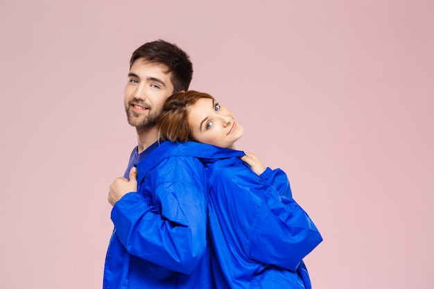 Funny young beautiful couple wearing one jacket  over light pink wall