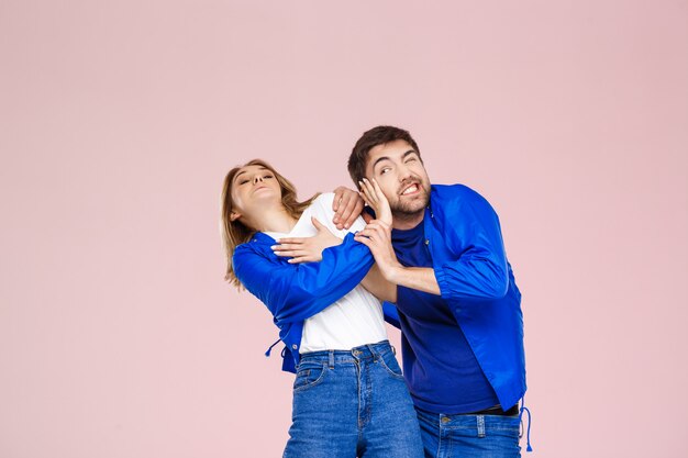 Смешная молодая красивая пара в пиджаке на светло-розовой стене