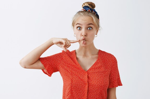 Funny young blond girl posing against the white wall