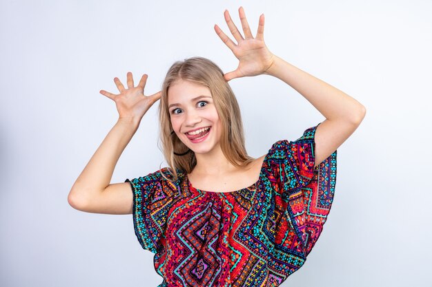 Funny young blonde woman putting hands on her head and gesturing horns with fingers 