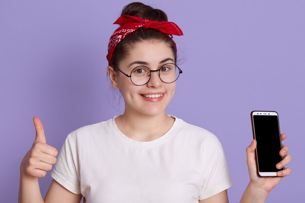 ライラックスペースに分離されたポーズの白いカジュアルなtシャツで面白い若いブルネットの女性少女