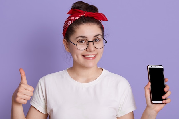 ライラックスペースに分離されたポーズの白いカジュアルなtシャツで面白い若いブルネットの女性少女