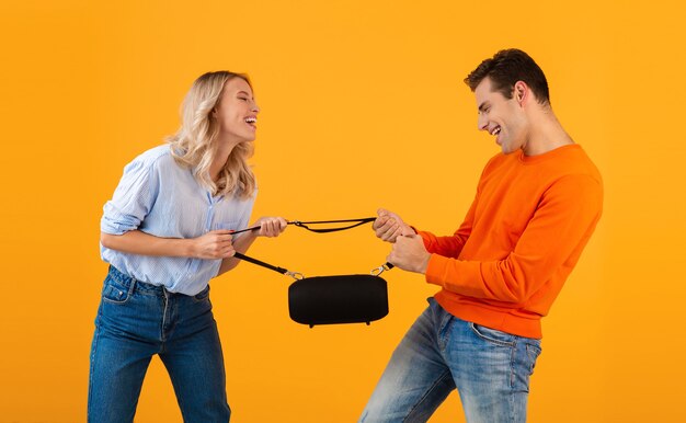 Funny young couple fighting for wireless speaker listening to music colorful style isolated on yellow