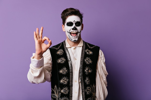 Funny young man shows sign ok. indoor portrait of guy with face painted for halloween.