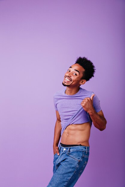 Funny young man with black hair taking off his shirt. blissful african guy playfully posing.