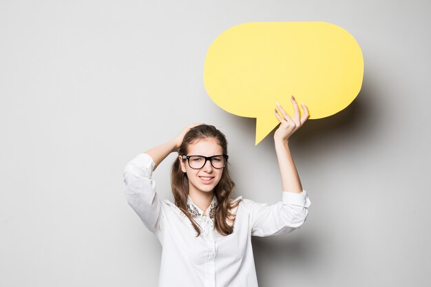 Funny young pretty student girl holds yellow chatting clouds over her head isolated on white background