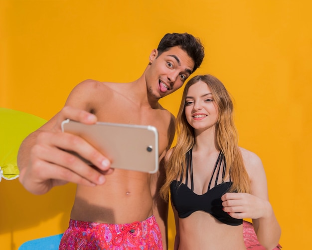 Смешные молодые возлюбленные в купальных костюмах делают селфи на телефоне в студии