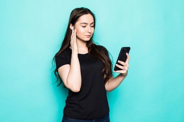 Funny young woman in casual white hoodie posing isolated on blue turquoise wall portrait. People lifestyle concept. Mock up copy space. Listen music with air pods, keeping eyes closed