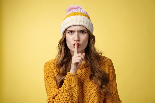 Furious angry annoyed cute woman shushing you irritated loud talk during important meeting frowning cringing pissed showing shhh gesture index finger pressed mouth, yellow background