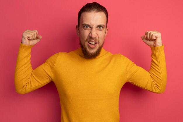 Free photo furious handsome blonde man keeps fists up on pink