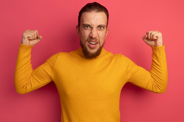 Furious handsome blonde man keeps fists up on pink