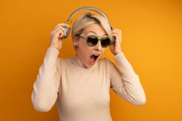 Furious young blonde girl wearing sunglasses taking off headphones screaming 