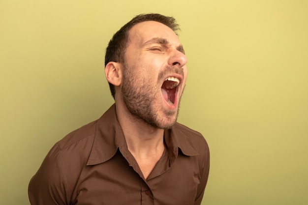 Furious young caucasian man screaming with closed eyes isolated on olive green background with copy space