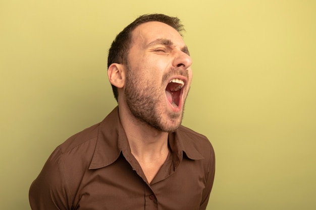 Foto gratuita giovane uomo caucasico furioso che grida con gli occhi chiusi isolati su priorità bassa verde oliva con lo spazio della copia