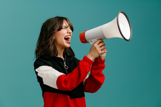 Free photo furious young caucasian woman standing in profile view looking at side shouting into loudspeaker isolated on blue background