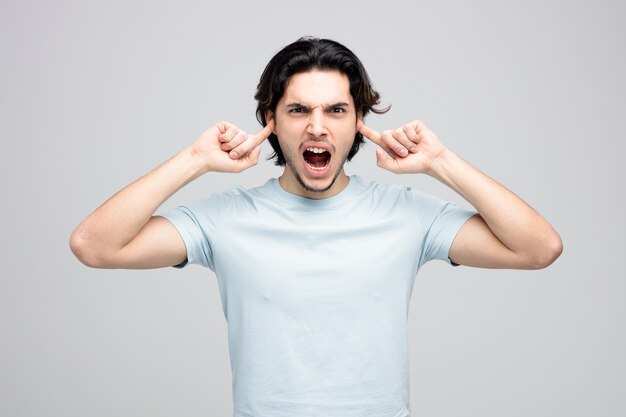 furious young handsome man looking at camera keeping fingers in ears screaming isolated on white background