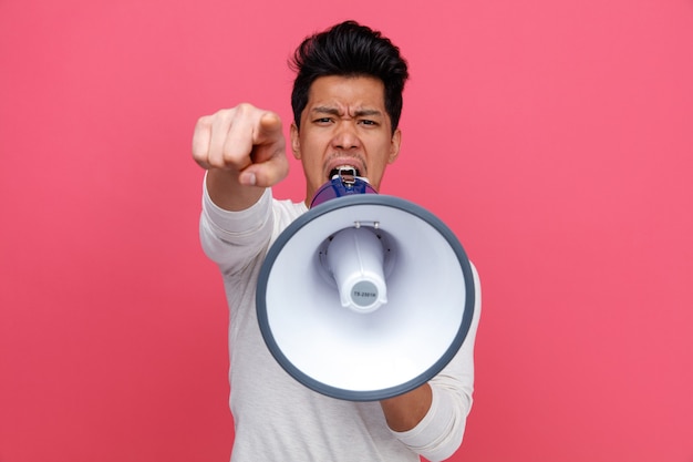 Furious young man looking and pointing at camera shouting in loud speaker 