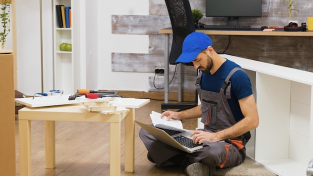 Furniture assembly worker uses laptop to consult instructions. Handyman doing a good job.