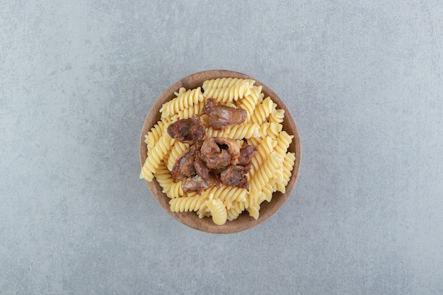 Fusilli and fried chicken in wooden bowl.