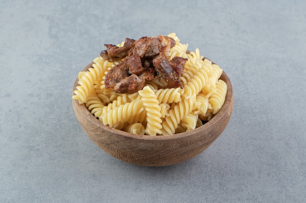 Fusilli and fried chicken in wooden bowl.