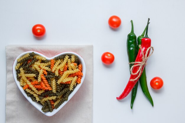 Fusilli pasta in a bowl with peppers, tomatoes top view on white and folded tablecloth table