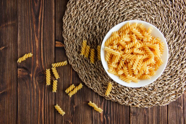 Fusilli pasta in a bowl on wooden and wicker placemat, flat lay.