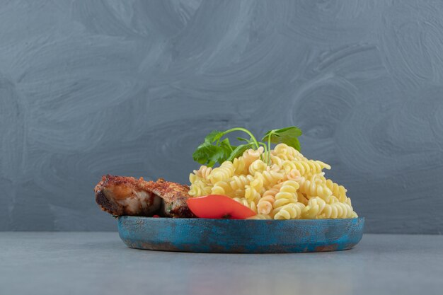 Fusilli pasta and chicken wing on blue plate.