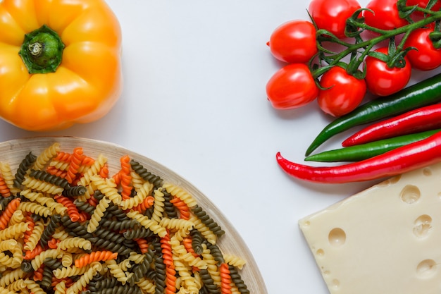 Pasta di fusilli in un piatto con i pomodori, peperoni, vista dell'angolo alto del formaggio su una tavola bianca