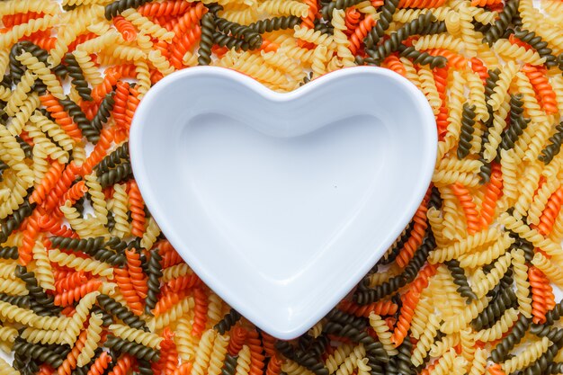 Free photo fusilli pasta with heart shaped bowl flat lay.