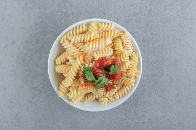 Fusilli pasta with ketchup in white bowl.