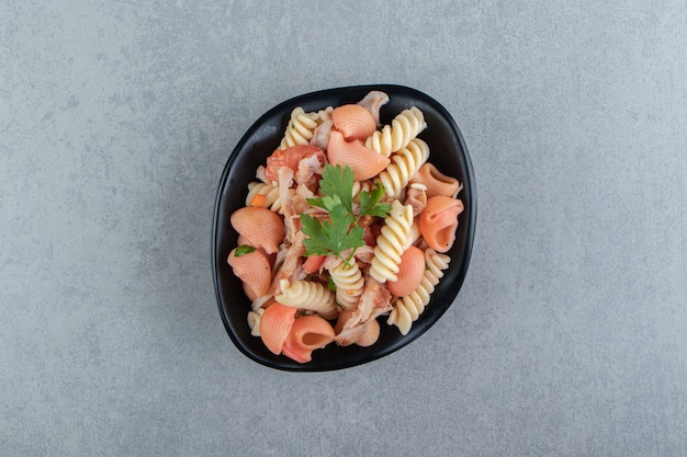 Fusilli and red seashell pasta in black bowl.