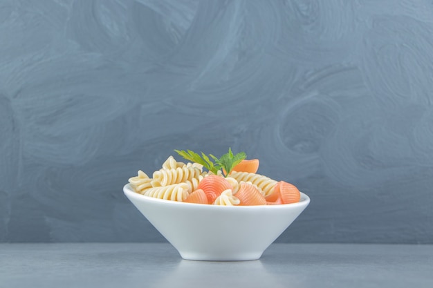 Fusilli and seashell pasta in white bowl.