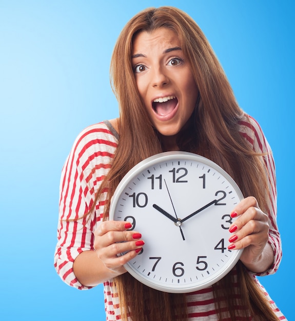 Fussy brunette hiding behind round white clock. 